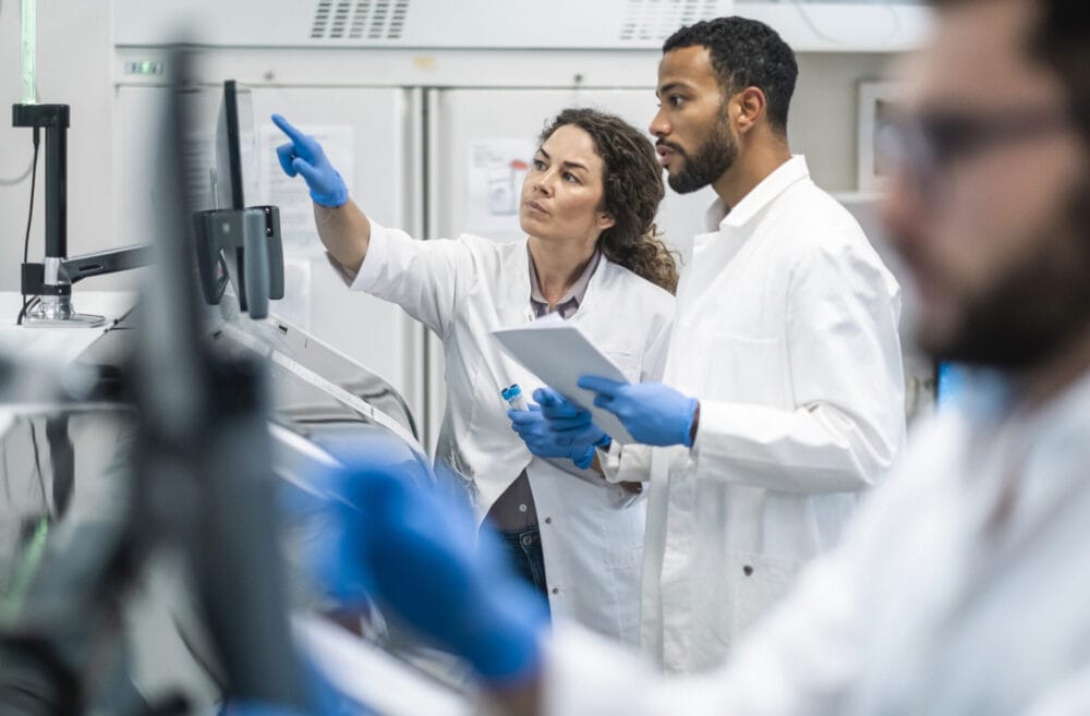 Two laboratory scientists in white coats reviewing results together
